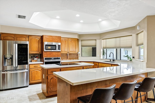 kitchen with brown cabinetry, a peninsula, a sink, appliances with stainless steel finishes, and a raised ceiling