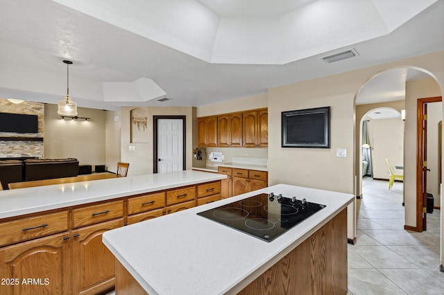 kitchen featuring brown cabinetry, a kitchen island, light tile patterned flooring, light countertops, and black electric cooktop