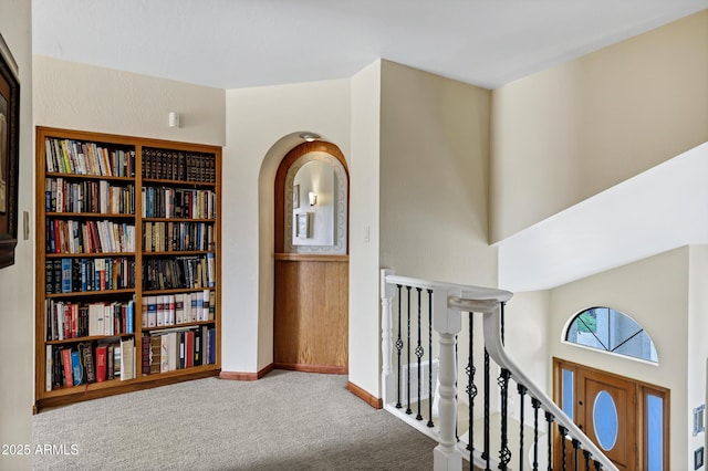 hall with an upstairs landing, baseboards, carpet floors, and arched walkways