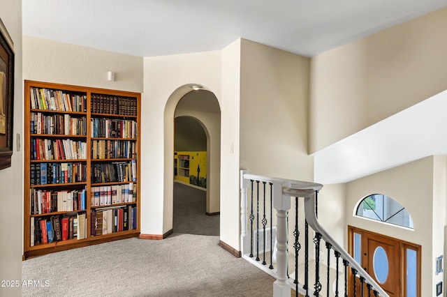 hall with an upstairs landing, carpet, arched walkways, and baseboards