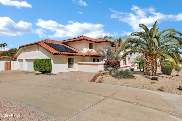 mediterranean / spanish-style house with solar panels, fence, a tile roof, stucco siding, and driveway