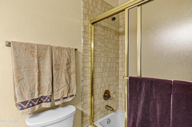 bathroom featuring toilet, a textured wall, and shower / bath combination with glass door