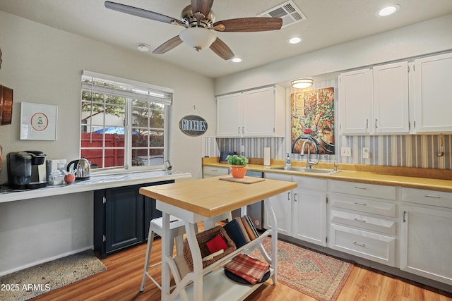 kitchen with white cabinets, ceiling fan, light wood-type flooring, and sink