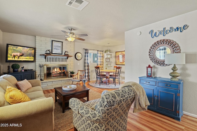 living room featuring a fireplace, a textured ceiling, light hardwood / wood-style flooring, and ceiling fan