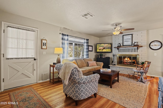 living room with ceiling fan, wood-type flooring, a textured ceiling, and a brick fireplace