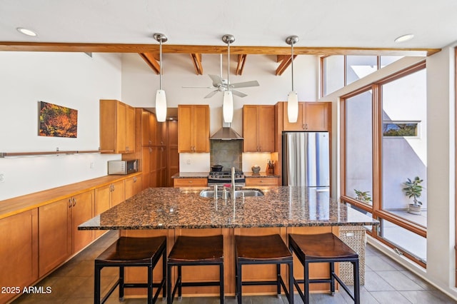 kitchen featuring a sink, wall chimney range hood, beam ceiling, freestanding refrigerator, and brown cabinetry