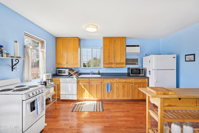 kitchen featuring white appliances, dark countertops, light wood-style flooring, a wall mounted air conditioner, and a sink