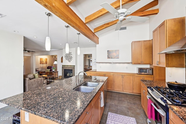 kitchen featuring a fireplace, stainless steel appliances, a kitchen island with sink, a sink, and wall chimney range hood