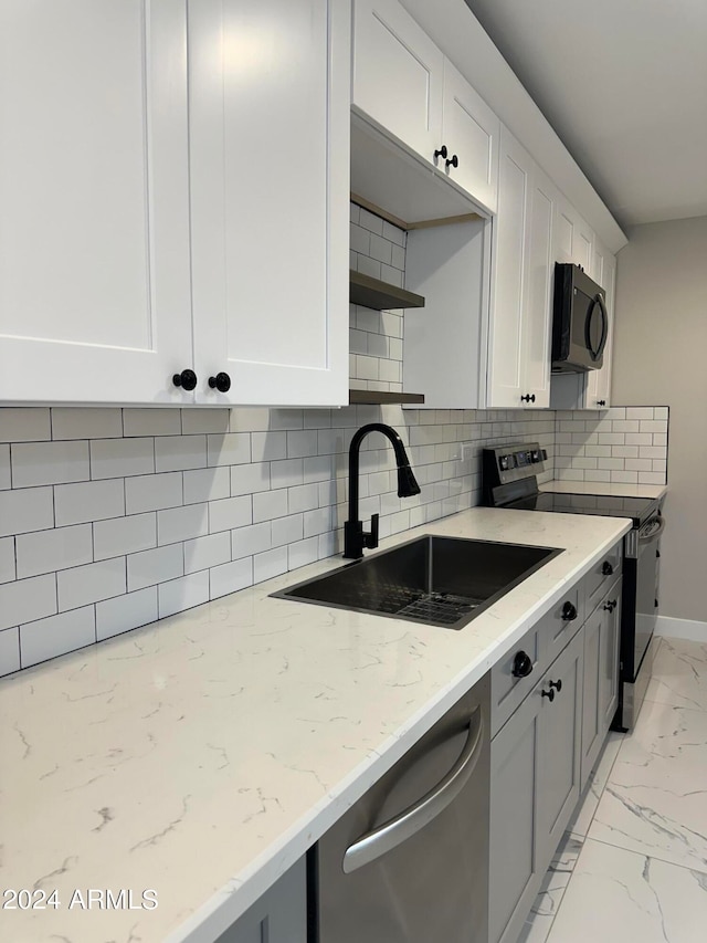 kitchen with light stone counters, sink, white cabinetry, stainless steel appliances, and decorative backsplash