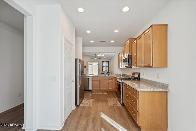 kitchen with stainless steel appliances, wood finished floors, light stone countertops, and recessed lighting