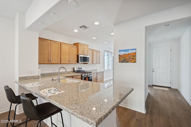 kitchen featuring light stone counters, dark wood-style flooring, a sink, visible vents, and appliances with stainless steel finishes