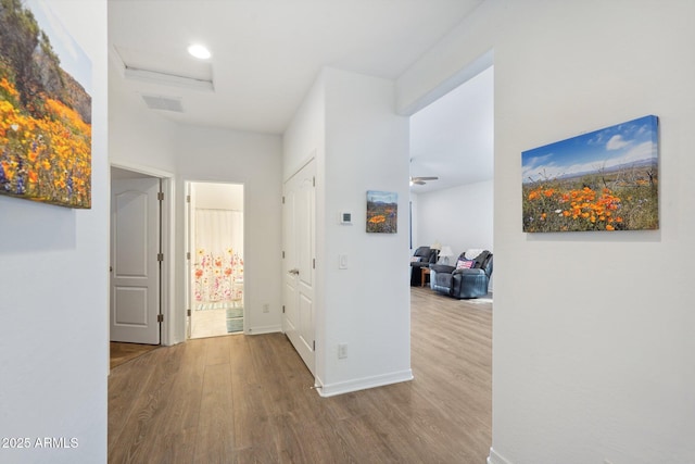 hall featuring baseboards, attic access, visible vents, and wood finished floors