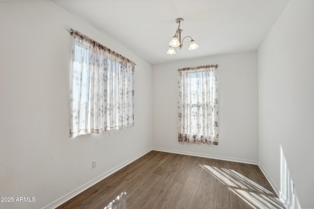 empty room with a notable chandelier, baseboards, and wood finished floors