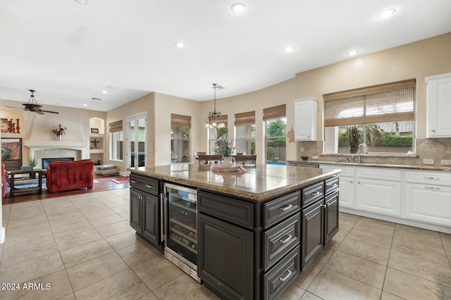 kitchen featuring a tile fireplace, a center island, wine cooler, decorative backsplash, and white cabinets