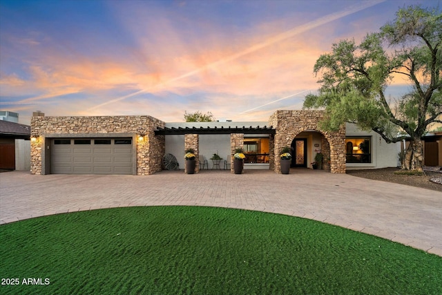 view of front of property with stone siding, an attached garage, decorative driveway, a front lawn, and stucco siding