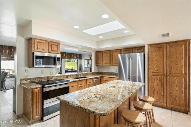 kitchen featuring visible vents, appliances with stainless steel finishes, brown cabinets, and light stone counters