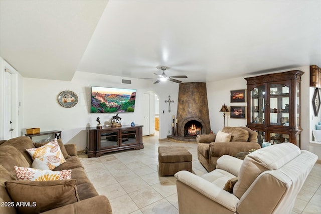 living room with a large fireplace, light tile patterned floors, arched walkways, and a ceiling fan