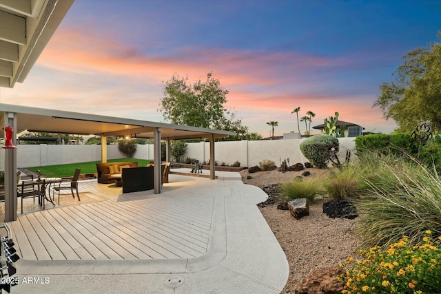 patio terrace at dusk with a fenced backyard, a deck, and an outdoor living space