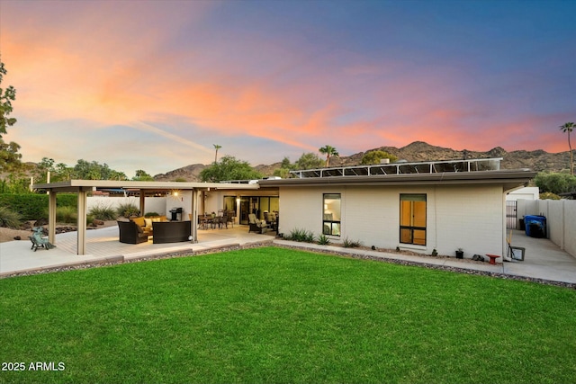 back of house at dusk with a lawn, fence, a patio area, a mountain view, and outdoor lounge area