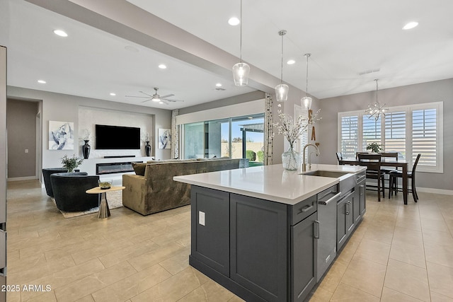 kitchen with ceiling fan with notable chandelier, an island with sink, sink, hanging light fixtures, and light tile patterned flooring