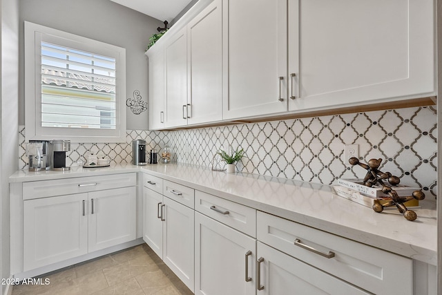 kitchen featuring white cabinets, backsplash, light tile patterned floors, and light stone countertops