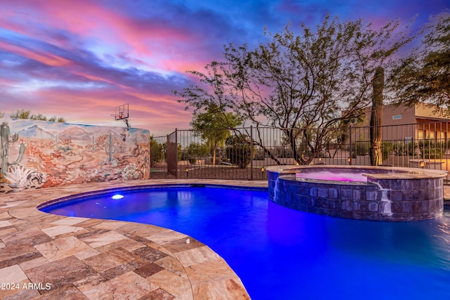 pool at dusk featuring a patio area and an in ground hot tub