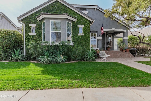 view of front facade featuring a tiled roof, a front yard, a patio, and stucco siding