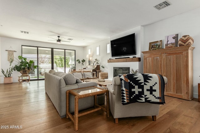 living room featuring light wood finished floors, a glass covered fireplace, and visible vents