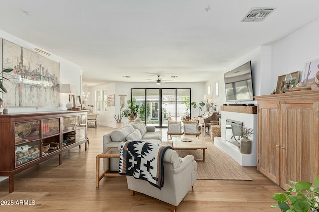 living room featuring a ceiling fan, visible vents, a fireplace with raised hearth, and light wood-style flooring