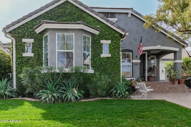 rear view of house with a tiled roof, a lawn, a patio area, and stucco siding