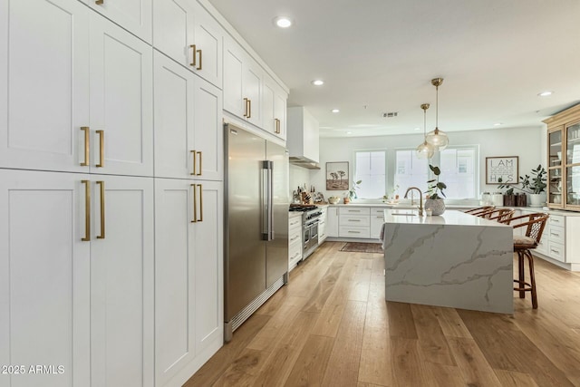 kitchen with light stone counters, pendant lighting, high end appliances, white cabinets, and a kitchen bar