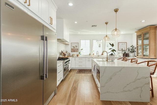 kitchen featuring light stone counters, premium appliances, white cabinetry, a kitchen breakfast bar, and decorative light fixtures