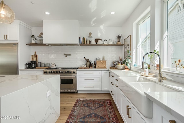 kitchen featuring appliances with stainless steel finishes, light stone countertops, white cabinetry, open shelves, and a sink