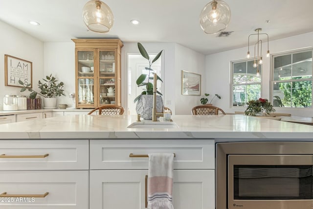 kitchen with light stone counters, white cabinets, stainless steel microwave, and visible vents