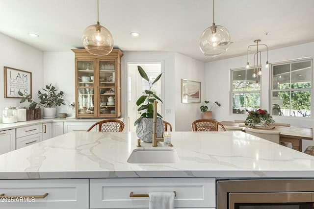 kitchen featuring white cabinets, a kitchen island, decorative light fixtures, and light stone countertops