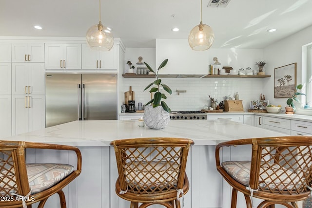 kitchen with a breakfast bar, built in fridge, white cabinets, and pendant lighting