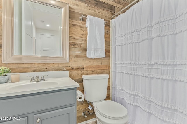 bathroom featuring toilet, wood walls, and vanity