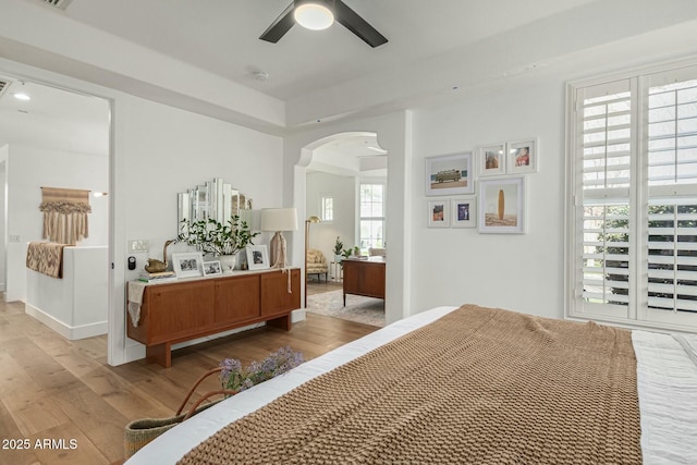 bedroom with light wood-style flooring, visible vents, arched walkways, and a ceiling fan