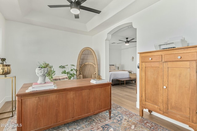 office with a tray ceiling, ceiling fan, arched walkways, and wood finished floors