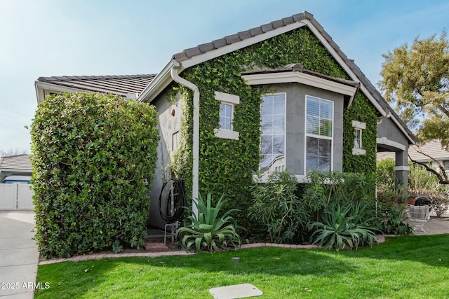 view of property exterior with a tiled roof, a lawn, and stucco siding