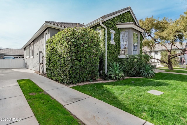 view of home's exterior with fence, a lawn, and stucco siding