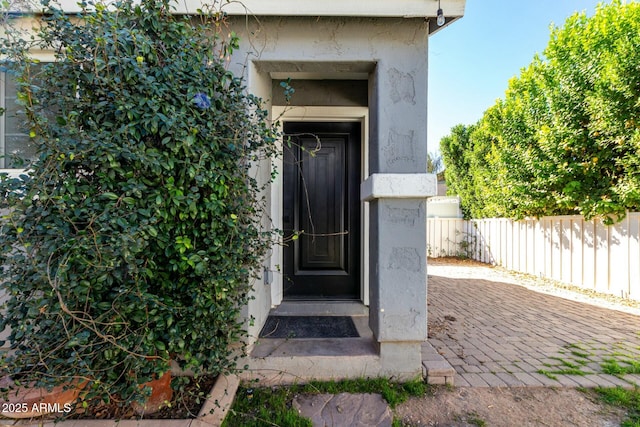 entrance to property featuring fence and stucco siding