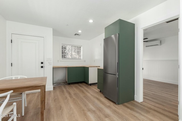 kitchen featuring light wood finished floors, visible vents, green cabinets, and an AC wall unit