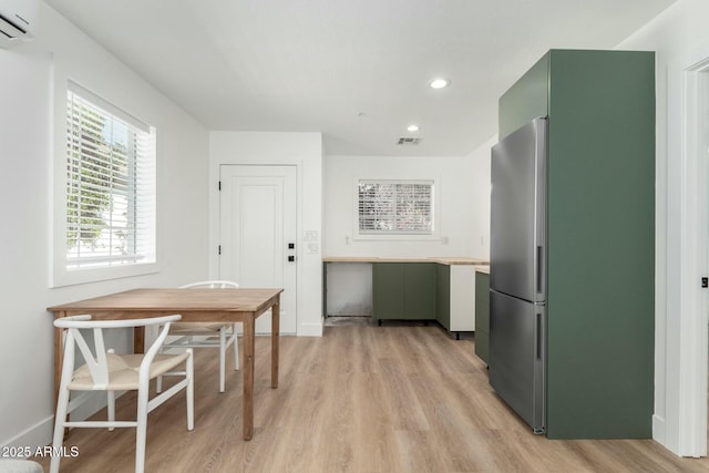 kitchen with visible vents, light wood-style floors, green cabinets, freestanding refrigerator, and a wall mounted air conditioner