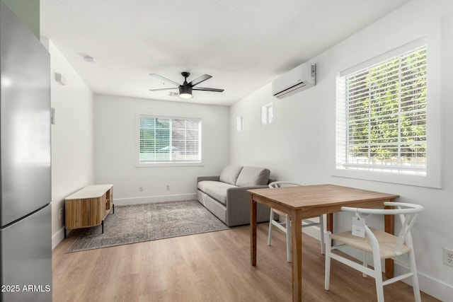 interior space featuring light wood-type flooring, a wall mounted air conditioner, ceiling fan, and baseboards