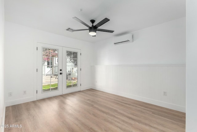 unfurnished room with light wood finished floors, baseboards, a ceiling fan, an AC wall unit, and french doors