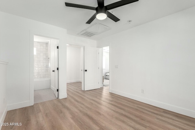 unfurnished bedroom featuring light wood-style flooring, attic access, ceiling fan, ensuite bath, and baseboards