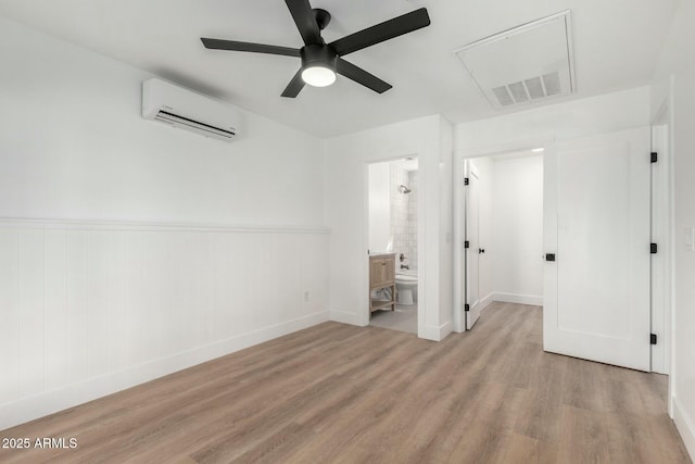 unfurnished bedroom with visible vents, ensuite bath, ceiling fan, light wood-style floors, and a wall mounted AC