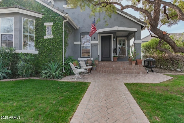 property entrance featuring a tiled roof, a lawn, and stucco siding