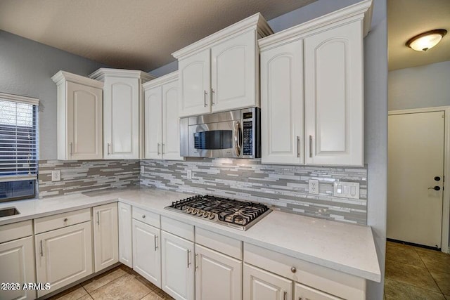 kitchen with tasteful backsplash, light tile patterned flooring, stainless steel appliances, and white cabinetry